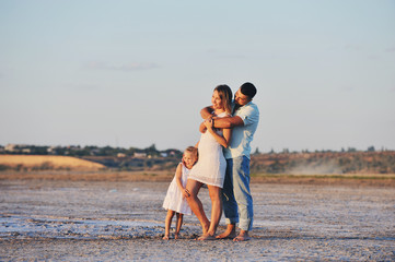 Молодые родители обнимают свою маленькую дочь на берегу моря - obrazy, fototapety, plakaty