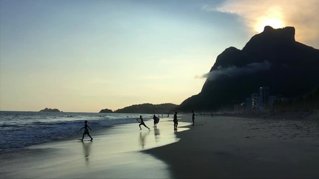 Silhouettes of body boarders running in slow motion on the sunset shore of Sao Conrado beach in Rio de Janeiro, Brazil