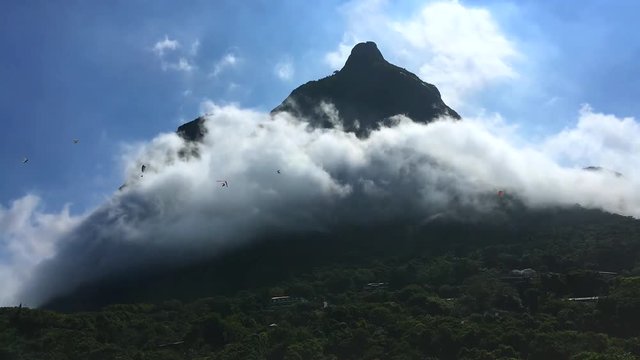 Hang gliders in timelapse buzzing like insects around Pedra da Gavea mountain viewed from Sao Conrado beach in Rio de Janeiro, Brazil