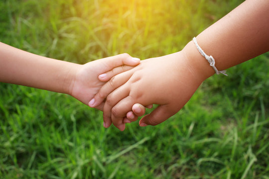 Children holding hands on the green grass with the sunlight