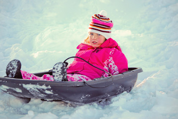 Fototapeta na wymiar Cute blue eyed girl on a sled in the snow.