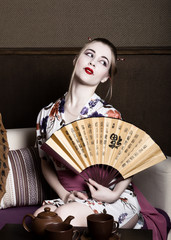 beautiful girl dressed as a geisha, she holds a chinese fan. Geisha makeup and hair dressed in a kimono. The concept of traditional Japanese values