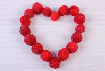 Heart of fresh raspberries on white wooden table, symbol of love