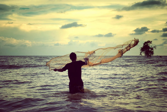 retro look image of a man throwing fishing net with sunset background
