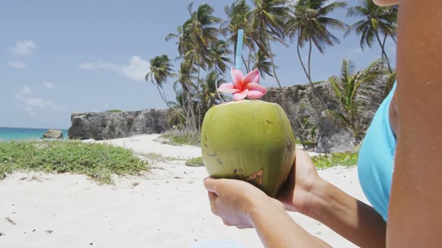 Fresh coconut water with straw on Caribbean beach in Barbados vacation. Unrecognizable woman in Barbados holding young green tropical fruit for healthy snack during summer holidays.