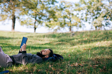 Bearded man hipster student reading a book and relax in park, exams