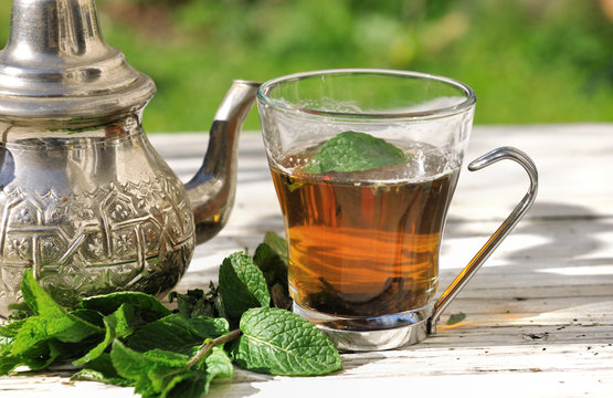 tasse de thé avec feuilles de menthe et théière sur table de jardin 