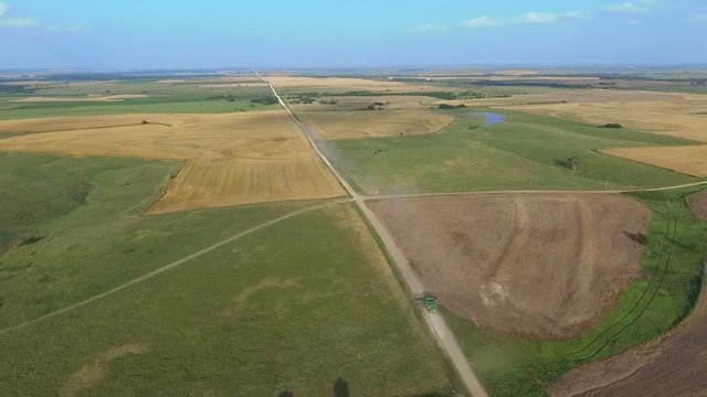 High aerial view of fields and roads as two combine harvesters move between wheat fields. 