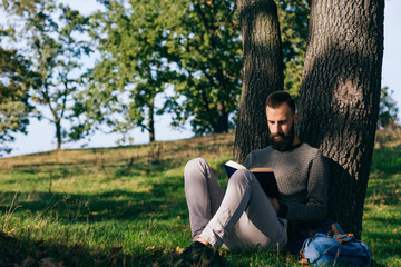 Bearded man hipster student reading a book and relax in park, exams