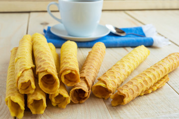Freshly honey waffles twisted into a tube on a wooden table and a cup of tea