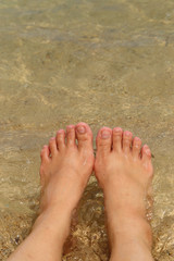 Female bare feet in sea water on sand beach.