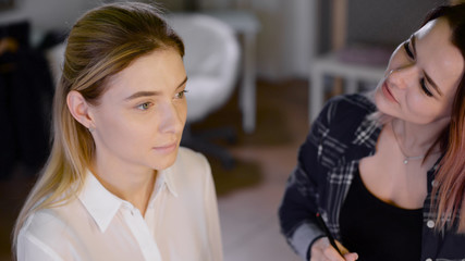 Young woman applying makeup to model in salon