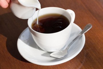 Pouring milk in a cup of black coffee