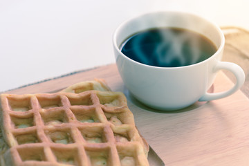 Hot coffee and waffle on wooden coaster.