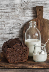 Chocolate cake, milk bottle, yogurt and cutting board on rustic wooden background