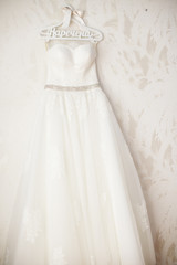 Fototapeta na wymiar Gorgeous stylish white wedding dress on hanger on wall