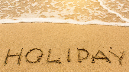 Fototapeta premium Holiday - inscription by hand on yellow beach sand.
