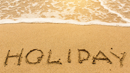 Holiday - inscription by hand on yellow beach sand.