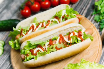 Hot dog with pickles, tomato and lettuce on wooden background