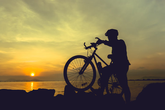 Healthy lifestyle. Silhouette of bicyclist standing with bike at seaside.