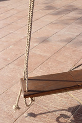 Wooden swing hanging on couple of ropes in warming sunlight.