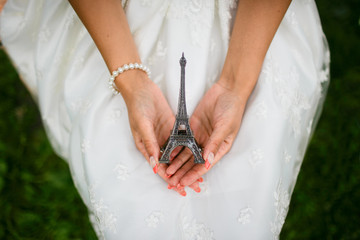 Obraz na płótnie Canvas Woman in white dress holding a figurine of the Eiffel tower. Miniature tower. On the hand bracelet of pearls. Souvenir from Paris