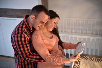Young smiling couple in love expecting a baby. They are looking at the baby clothes. 