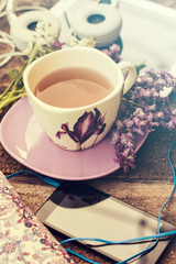 still life with tea cup and the contents of a work space composed. Different objects on wooden table. tablet,phone with headphones and spring flowers