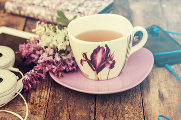 still life with tea cup and the contents of a work space composed. Different objects on wooden table. tablet,phone with headphones and spring flowers