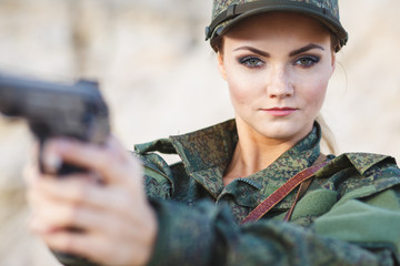 Gorgeous young woman in a Military costume with a gun on the background of a dessert