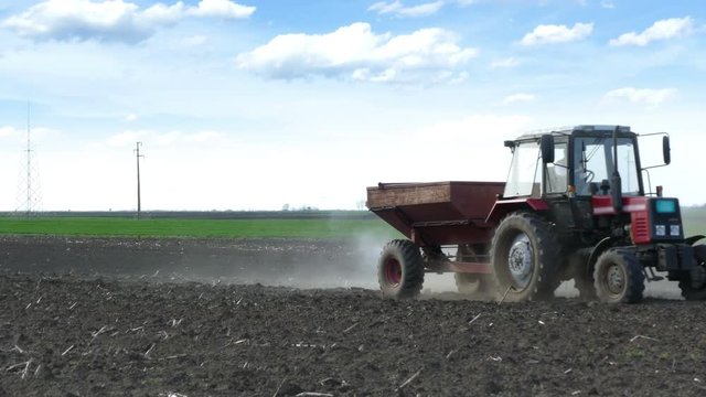 Tractor and fertilizer spreader on the field, scattering mineral fertilizers before sowing to increase crop yields