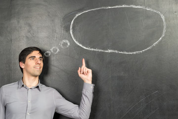 Young instirated man standing nearly chalkboard background and pointing speech bubble