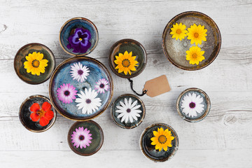 Festive colorful flowers floating in handmade ceramic bowls with empty gift tag. Top view with copy space