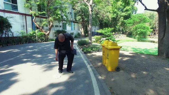 Fat bald head Asian Thai man find litter on the road and put it in the trash can like a good citizen in 4k ultra hd