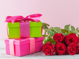 Red roses and gift boxes on wooden table with pink background and copy space.