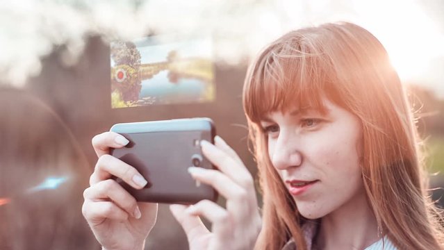 Girl shooting video with a smartphone camera with hologram, that appears at the top of the smartphone. Technology concept.