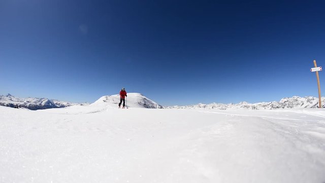 Alpinist ski touring on the ridge with expansive snowcapped mountain view in a bright sunny day. One person hiking towards the camera. Italian French Alps.