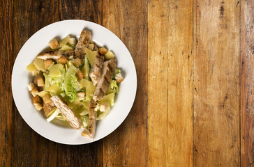 Caesar salad with croutons and grilled chicken on wooden table