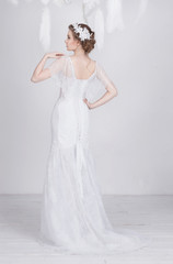 Fototapeta premium Elegant young and dreamy beautiful bride in a luxurious lace wedding dress. She has lace decoration in her beautiful dark blond hair. She is elegant and delicate. The dress has lacing on the back.
