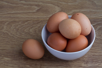 A white bowl full of fresh, brown, speckled eggs on a wooden table.