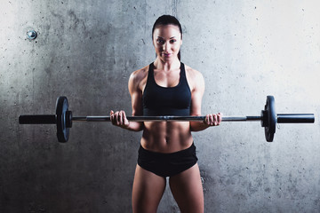Fototapeta na wymiar Beautiful muscular woman doing exercise with barbell on a gray background.