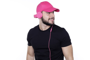 Junger Mann mit schwarzem T-Shirt und pink Kopfhörern und Basecap hört Musik