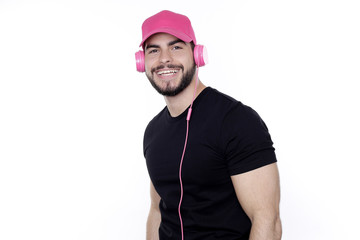 Junger Mann mit schwarzem T-Shirt und pink Kopfhörern und Basecap hört Musik und lächelt in die Kamera