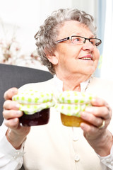 Babcine przetwory, smakowite konfitury. Starsza kobieta ze słoikami  własnoręcznie przygotowanych dżemów.