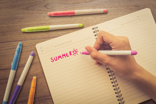 Female writing "summer" on notebook