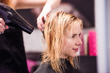 Naklejka premium Unrecognizable hairdresser drying hair of her beautiful young cl