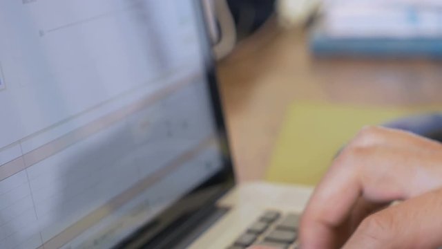 Man typing on a laptop using keyboard and mouse while working on a spreadsheet