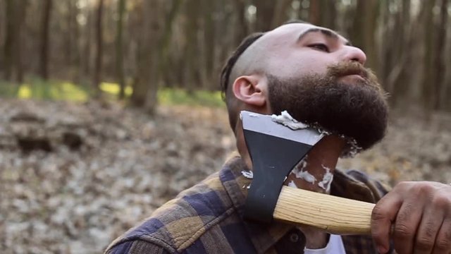 bearded lumberjack has a shave with an axe