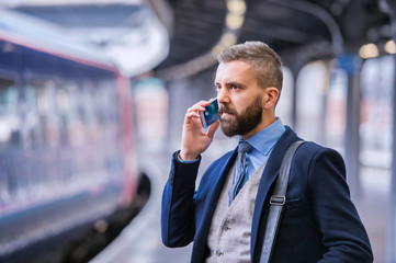 Businessman with smartphone, making a phone call, train platform