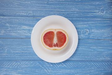 half a grapefruit on white plate on blue wood background